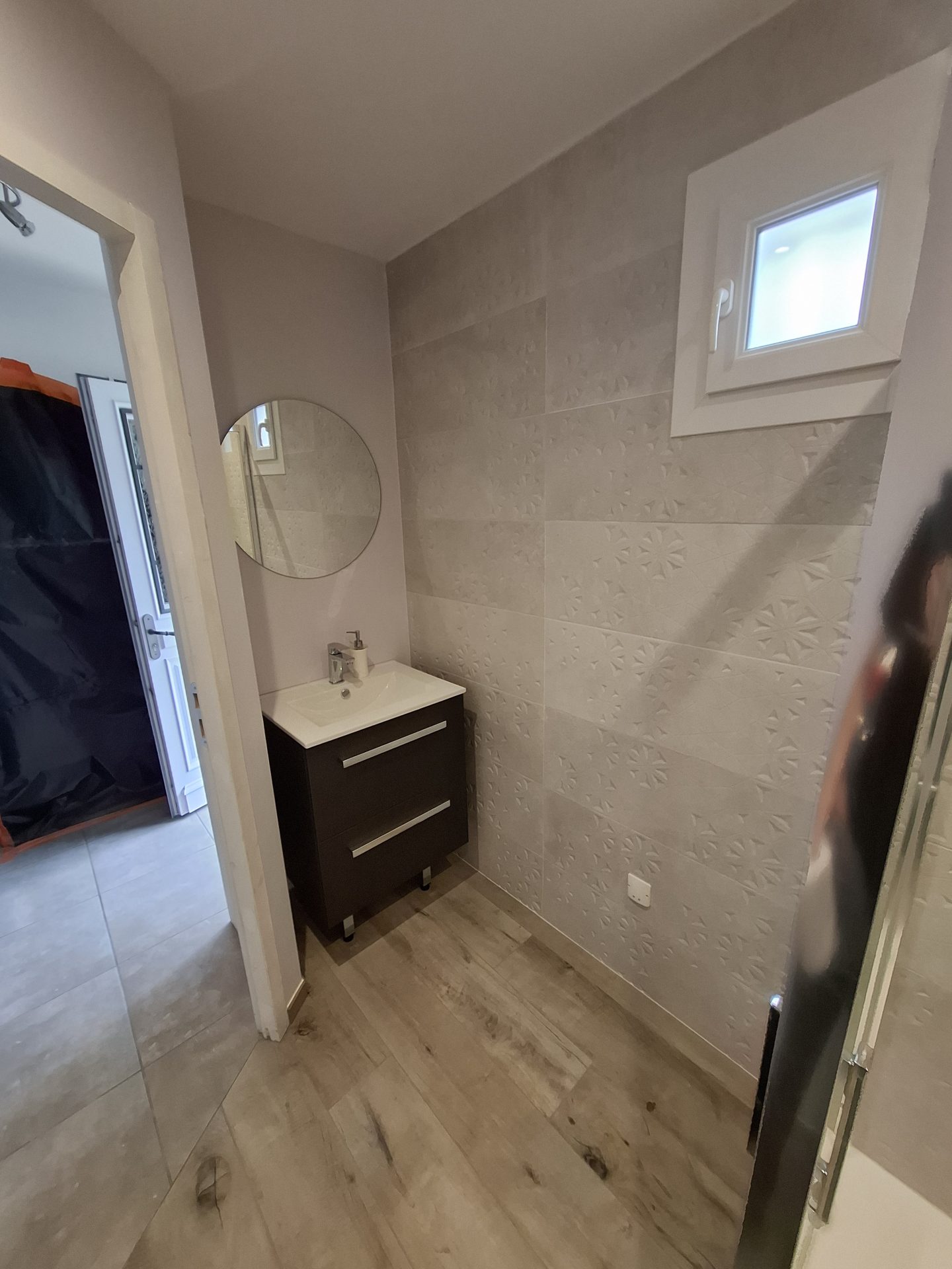 Pose d'une vasque suspendue et d'un miroir rond lors d'une rénovation de salle de bain moderne réalisée par l'entreprise Jimmy Paul à Pau.