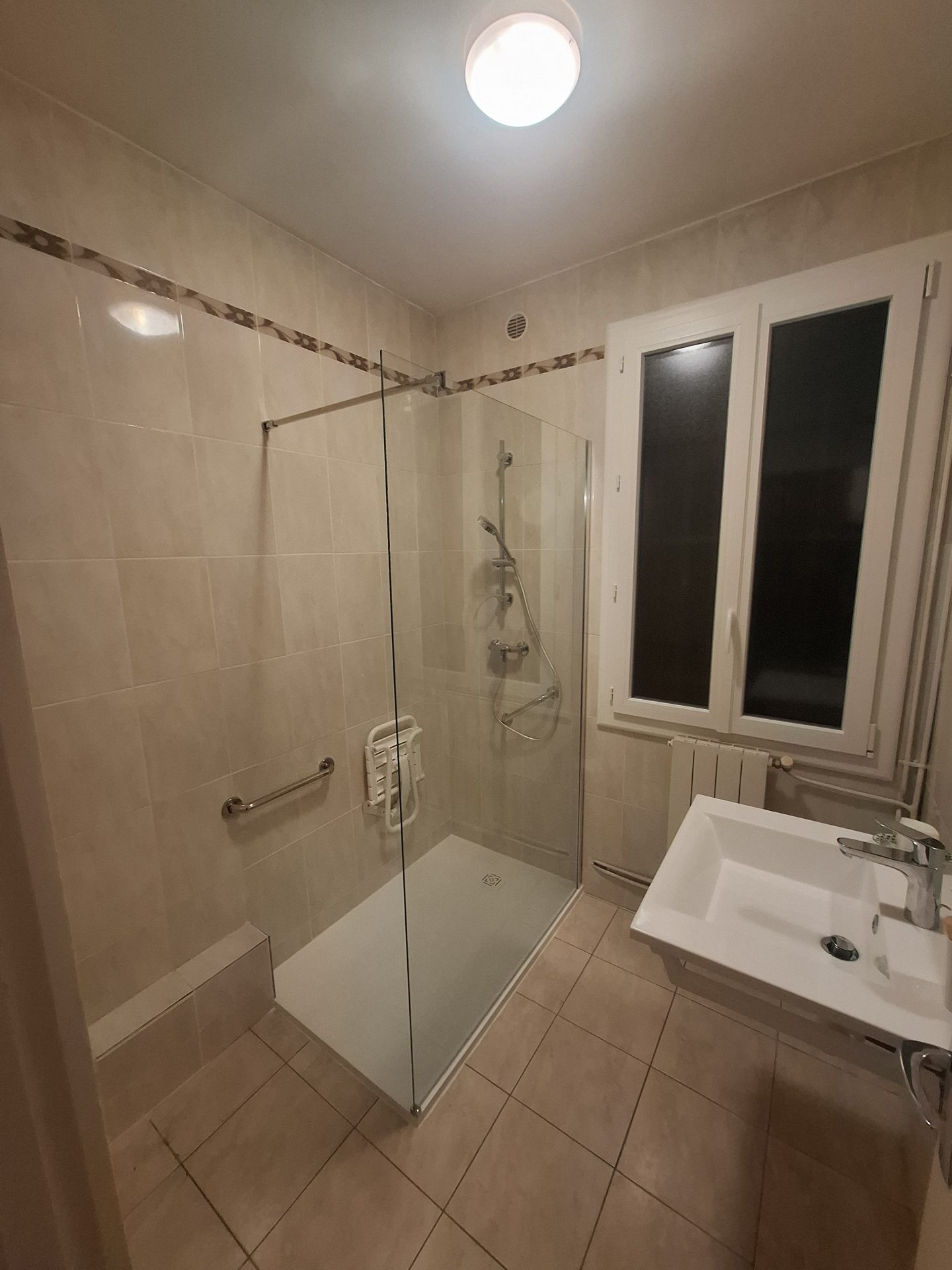 Rénovation de salle de bain pour PMR à Lescar par Jimmy Paul, incluant une douche avec siège, une paroi en verre et un meuble vasque suspendu.