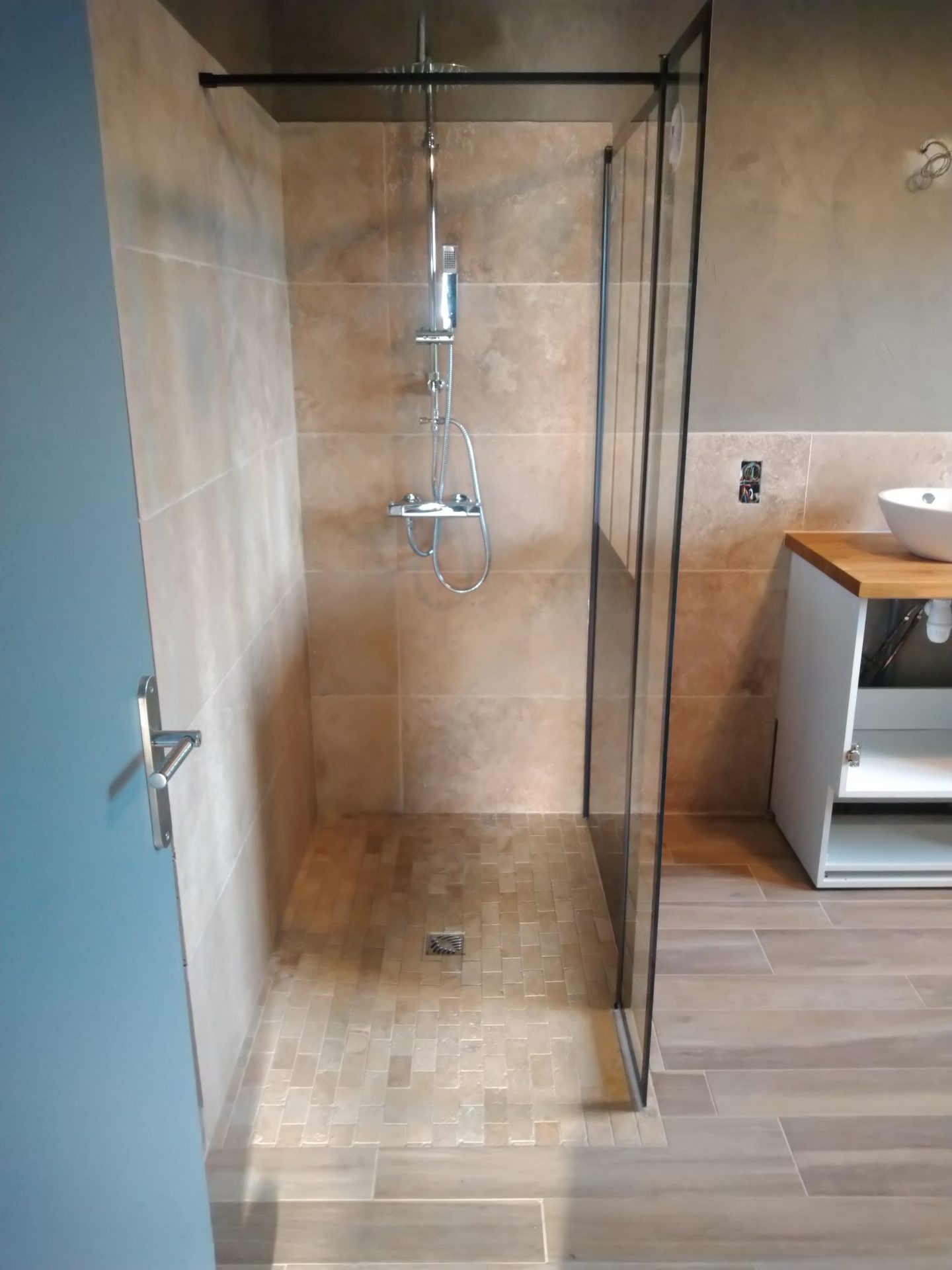 Douche à l'italienne habillée de pierre naturelle beige et robinetterie chromée, réalisation d'une rénovation de salle de bain par la société Jimmy Paul à Morlaàs.
