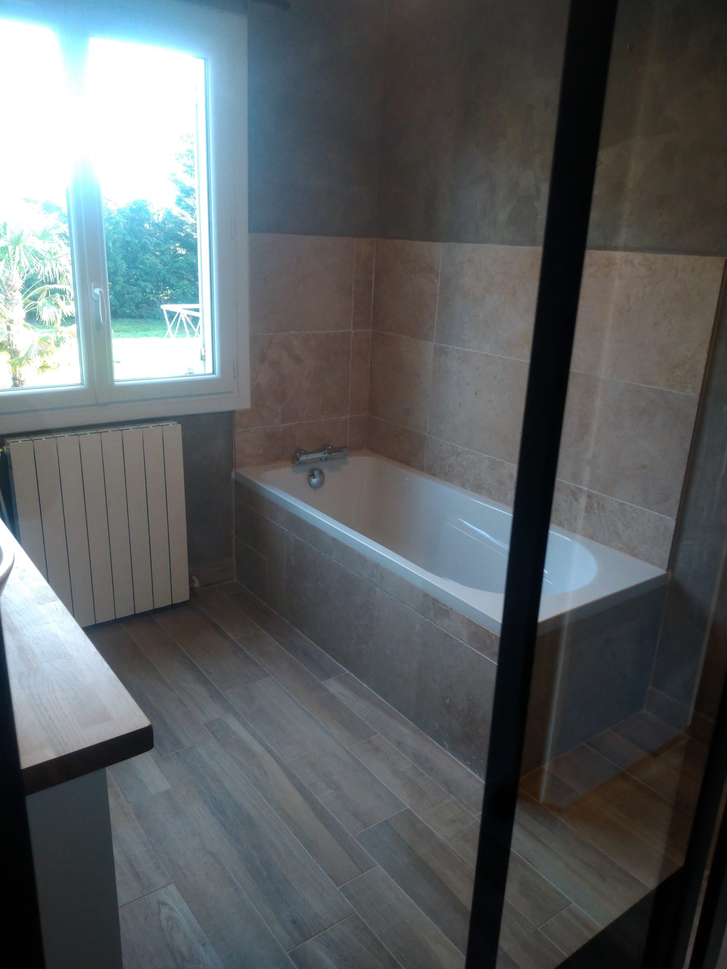 Pose d'une baignoire entourée de carrelage en pierre naturelle beige, finitions parfaites d'une rénovation de salle de bain par Jimmy Paul à Lons.