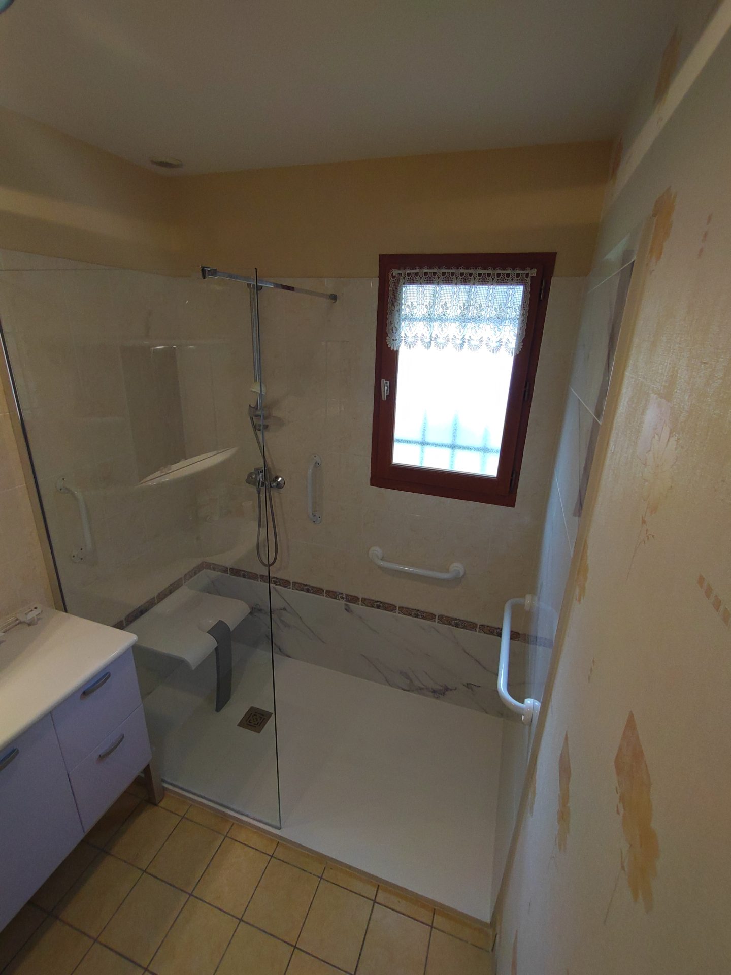 Aménagement sécurisé avec douche à l'italienne, siège rétractable et poignée PMR, travaux de rénovation de salle de bain effectués par Jimmy Paul à Lescar.