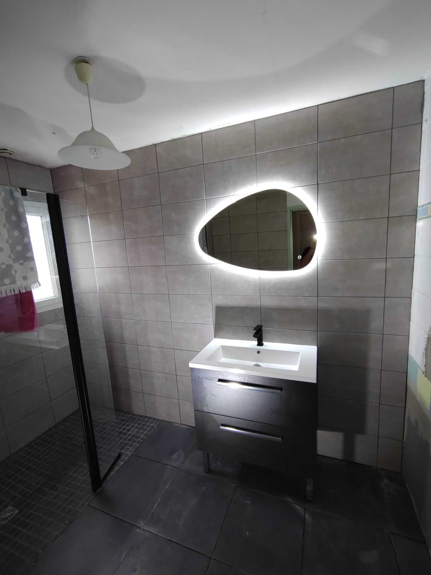 Fixation d'un meuble vasque sur pied moderne surmonté d'un miroir rétroéclairé, détail chic d'une rénovation de salle de bain par Jimmy Paul à Idron.