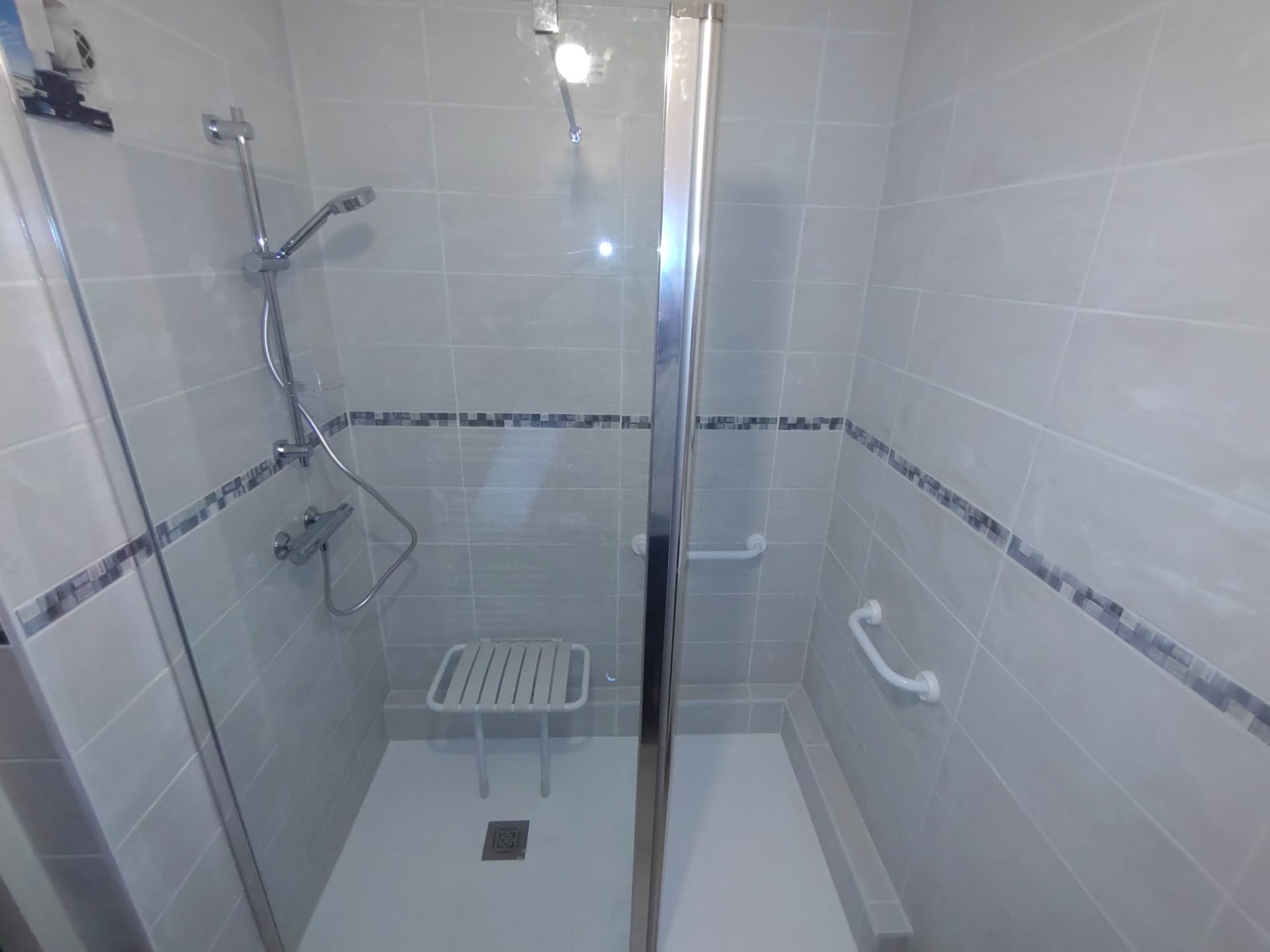 Création d'une grande douche carrée accessible avec siège rétractable et poignée pour personnes à mobilité réduite, une rénovation de salle de bain signée Jimmy Paul à Lescar.